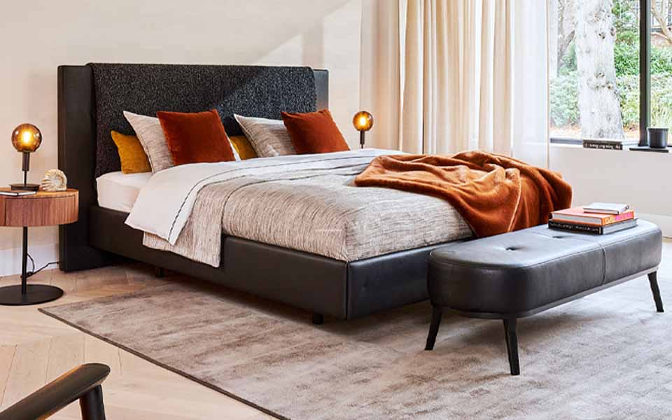 Doppelbett mit schwarzem Rahmen, heller Bettwäsche und hellbraunen Kissen