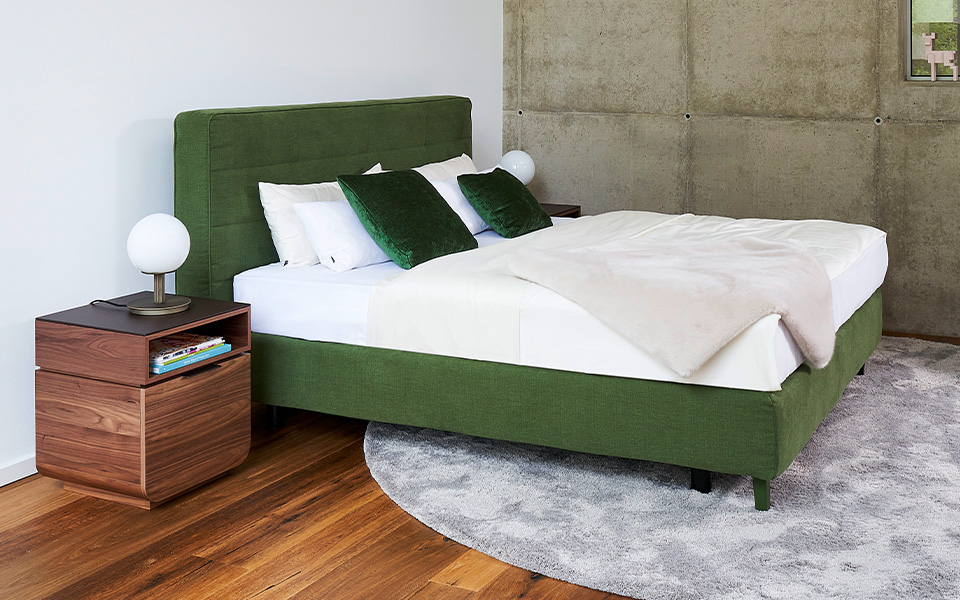 Dunkelgrünes Bett mit weißer Bettwäsche und dunkelgrünen Kissen