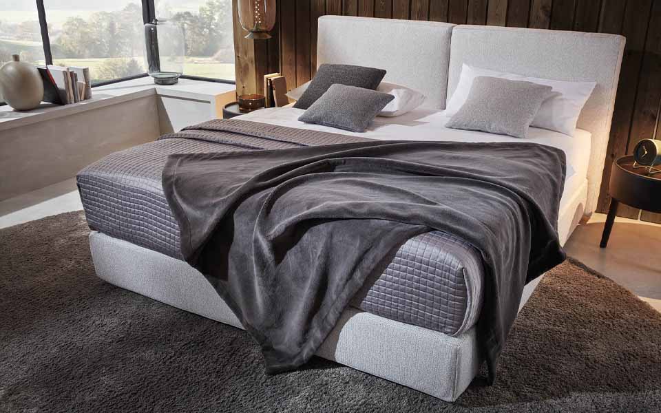 Helles Bett mit Kopfkissen und Decken in verschiedenen Grautönen