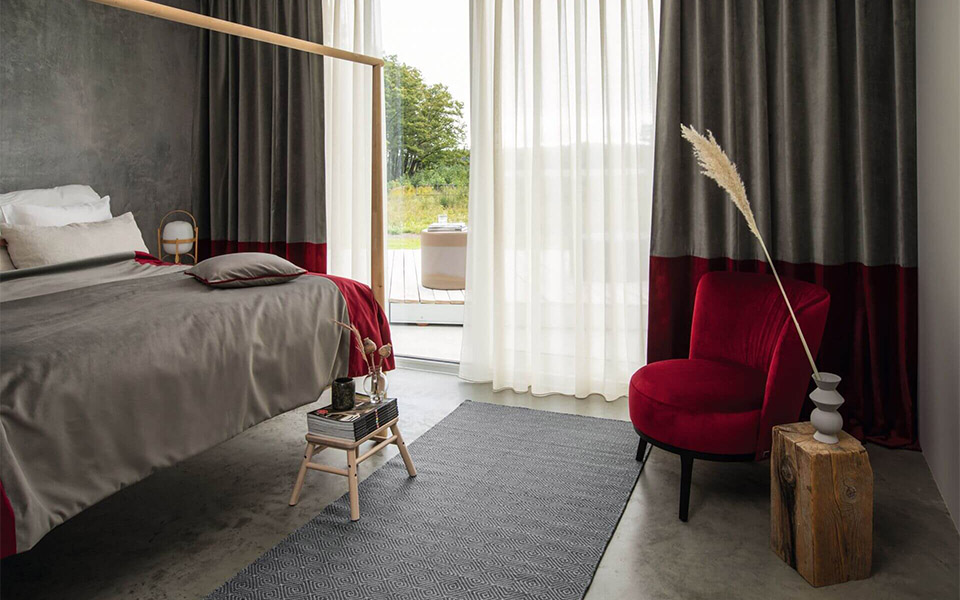 Cremefarbene Flächenvorhänge und modernes Bett mit hochwertigem Stoffbezug im Schlafzimmer
