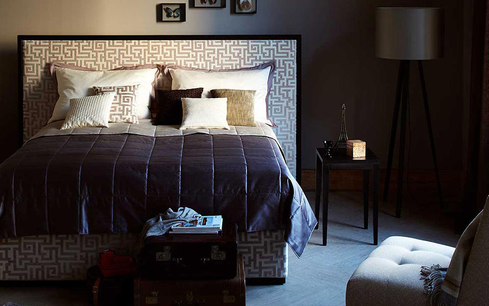 Helles Bett mit Tagesdecke und gemusterten Polstern