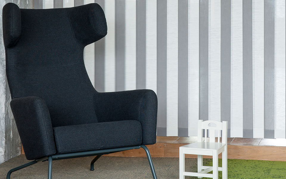 Grau-weiße Lamellen vor einem schwarzem Sessel und kleinem Stuhl